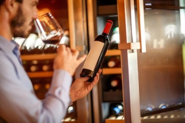 man drinking wine in front of a wine cooler